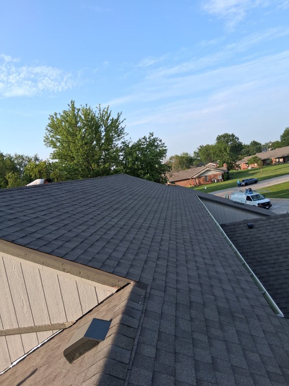 Completed gray shingle roof replacement surrounded by trees